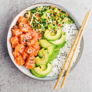 A poke bowl with salmon, guacamole, and rice in teh bowl. Chop sticks are placed on top of the bowl.